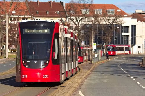 Rote Straßenbahn fährt an einer Haltestelle in Nürnberg los, im Hintergrund fahren zwei weitere Straßenbahnen
