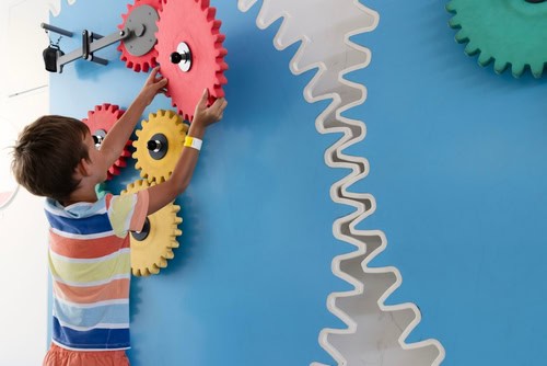Kind spielt mit bunten Zahnrädern, die an einer Wand installiert sind