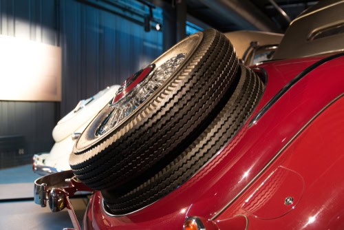Nahaufahme eines Ersatzrades auf dem Heck einen roten Oldtimers, der in einer Halle steht
