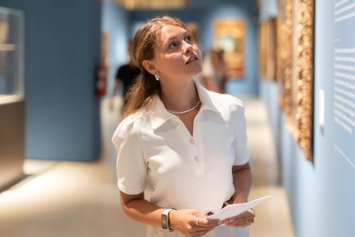 Junge Frau mit einer Informationsbroschüre vor der Infotafel in einem Museum