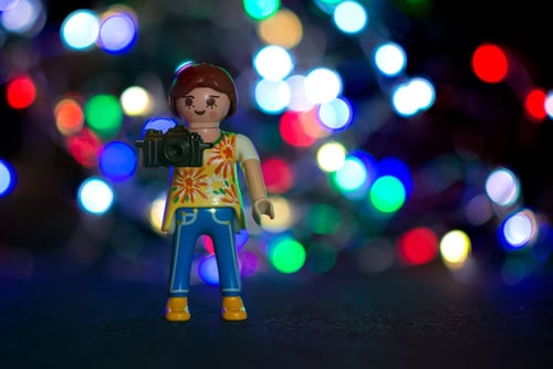 Playmobilfigur mit Kamera und unscharfen, bunten Lichtern im Hintergrund